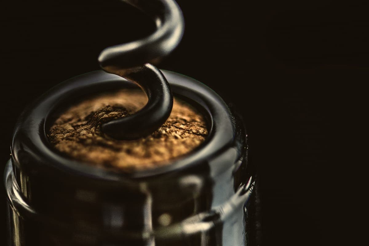 A corkscrew turned into the cork of a dark wine bottle, close up, against black.