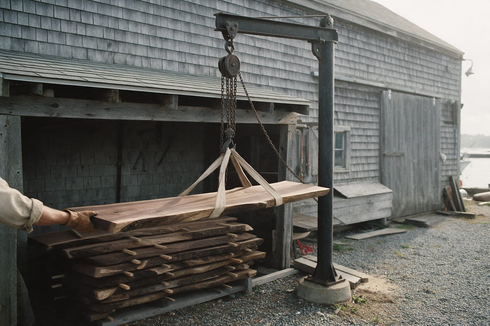 The old jib crane in the yard lifting a walnut slab off the stack