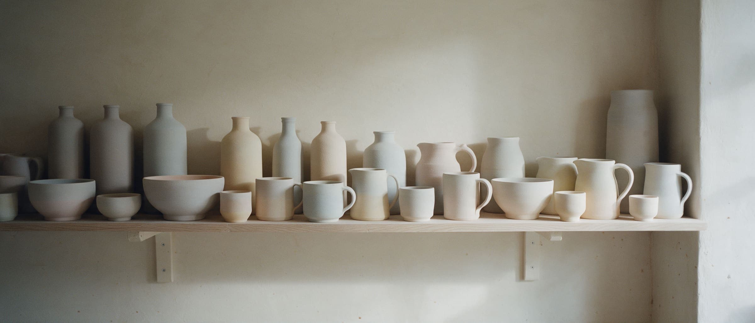 Glazed, unfired pots lined up on a long ware board