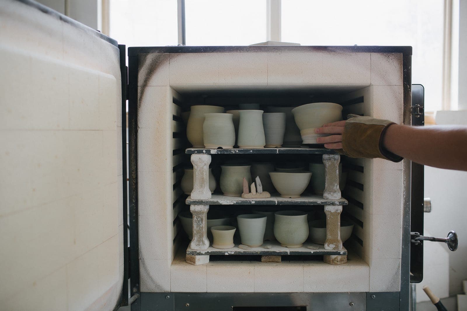 A gloved hand sliding the last shelf into the loaded kiln