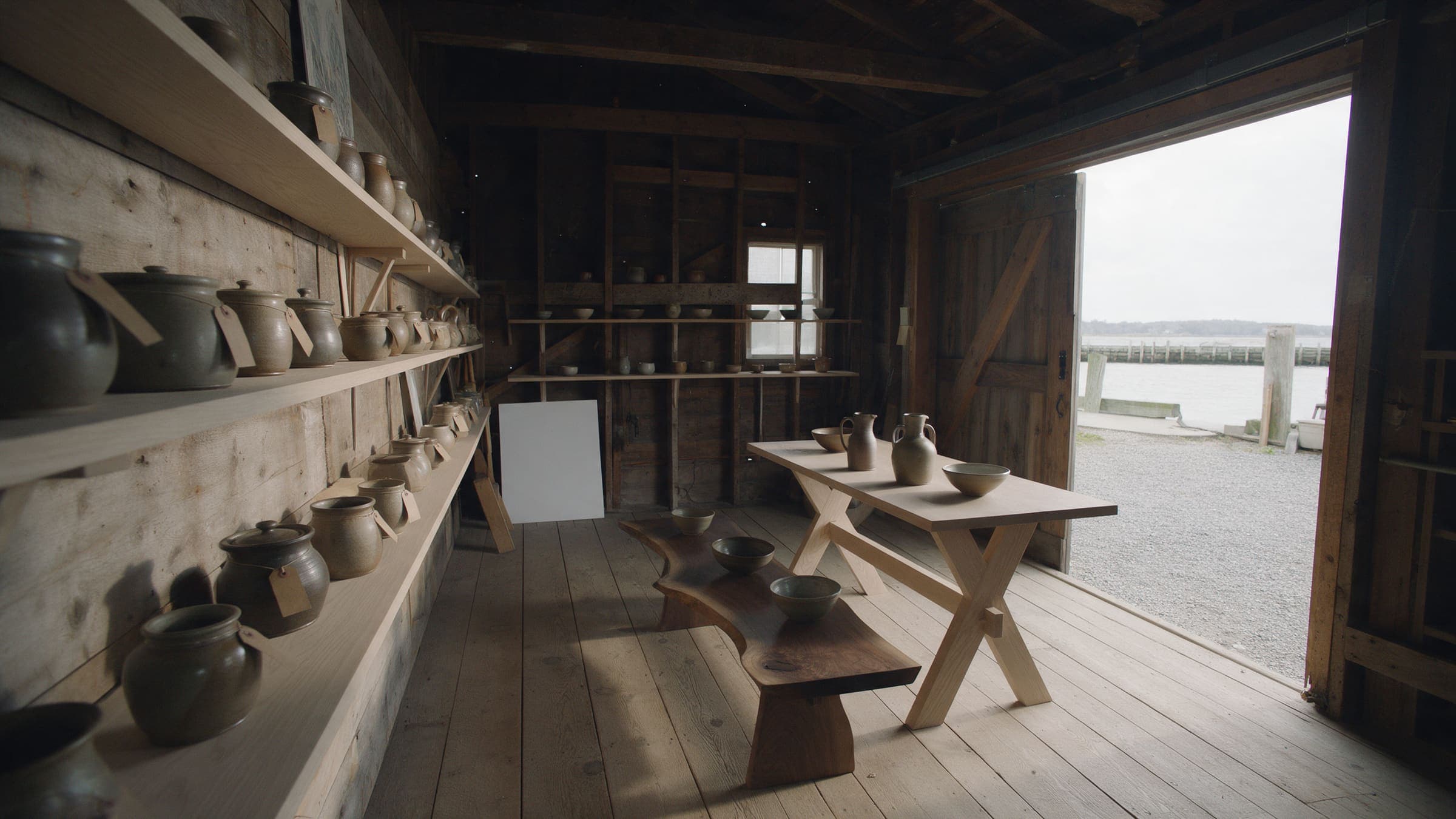 Inside the shop: tagged pots on oak shelves, a walnut bench and a trestle table, the door open to the harbor