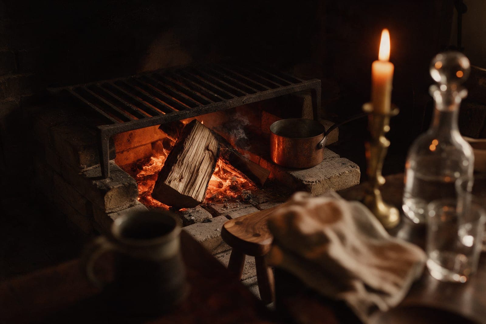 Split oak collapsing into embers inside the hearth, cherry wood smoking at the side, the cast-iron grate above.