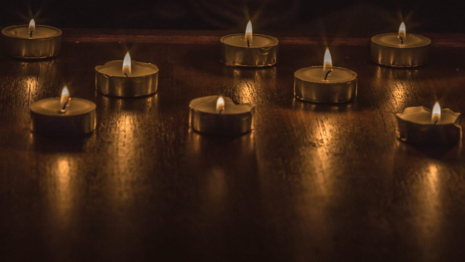 Small candles burning on a dark wooden table, their light pooled on the grain.