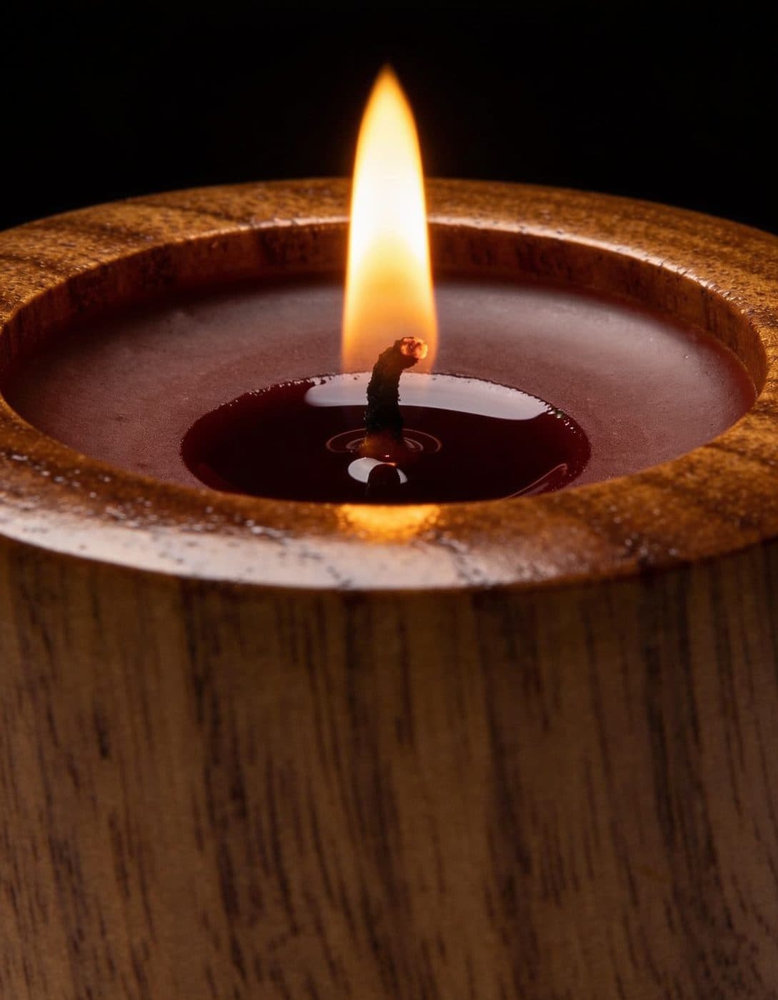 A candle burning low in a turned walnut cup, the wax pooled around the wick.