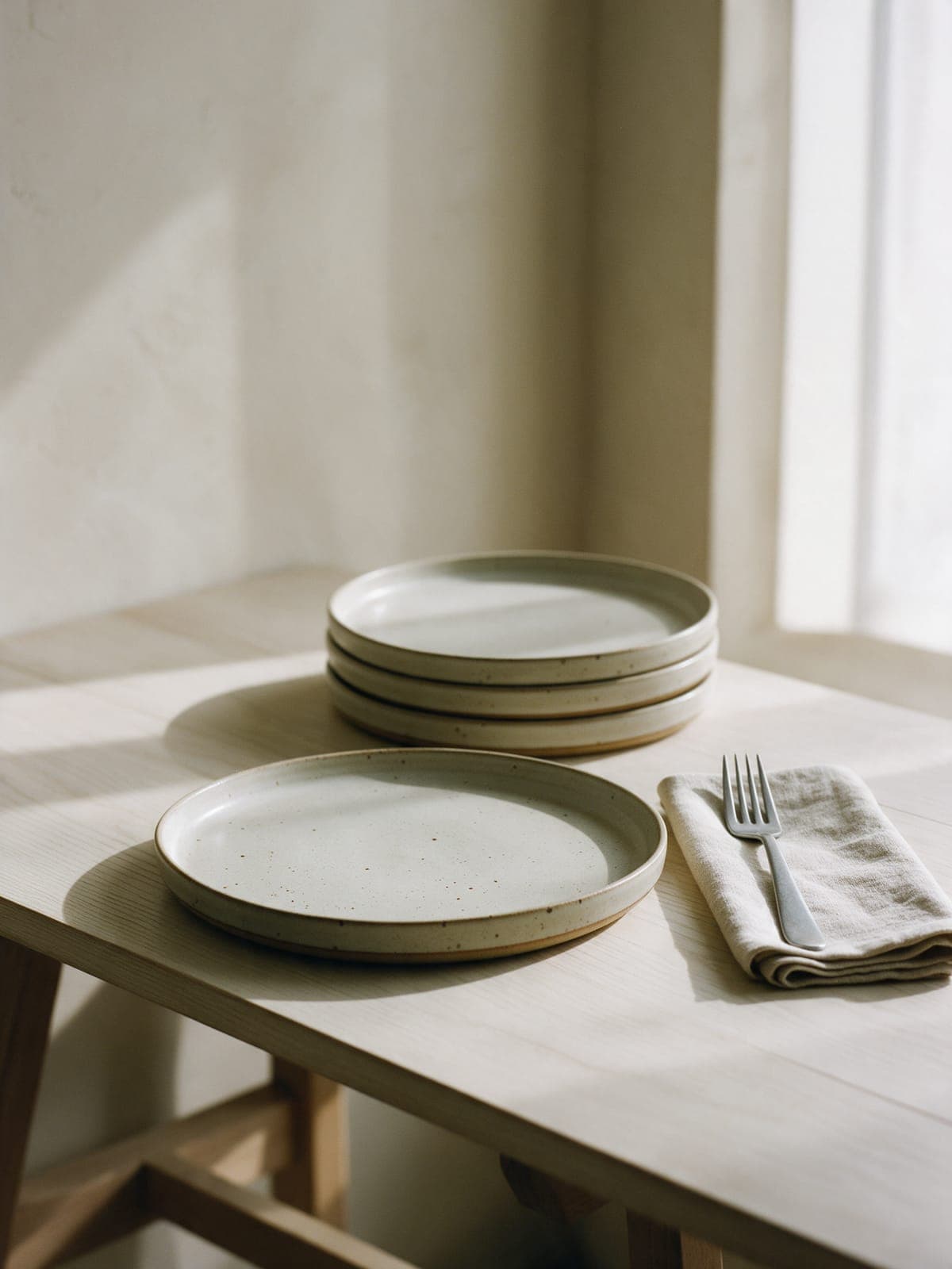 A speckled dinner plate set on an oak table with a linen napkin