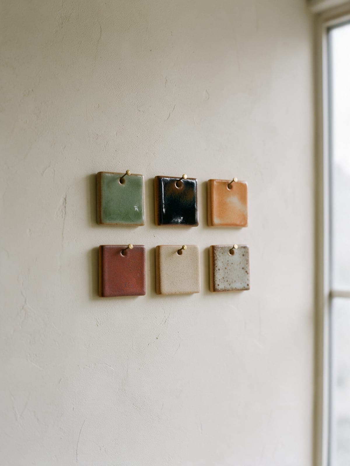 Six glazed tiles hung in two rows on a plaster wall