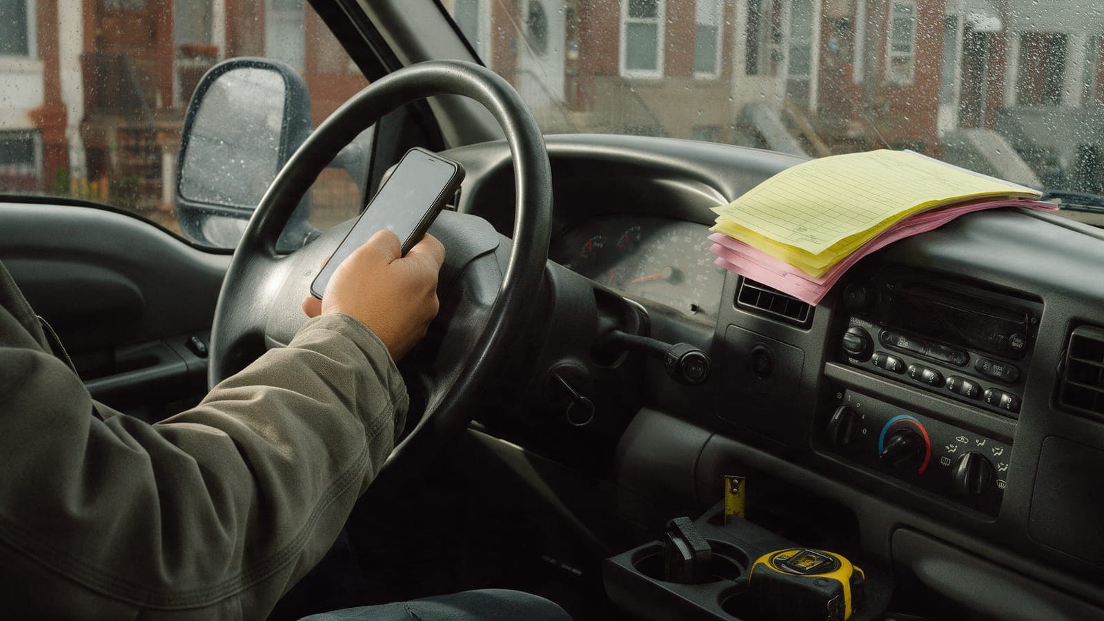 A technician's hand holding a phone in a truck cab, a yellow carbon pad on the dashboard.