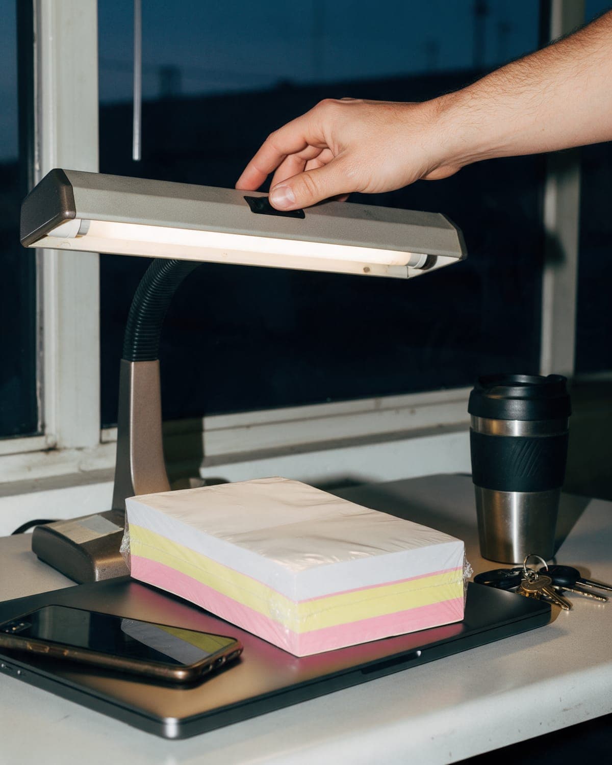 A hand switching on a desk lamp before dawn over a new three-part carbon pad still in its shrink wrap.