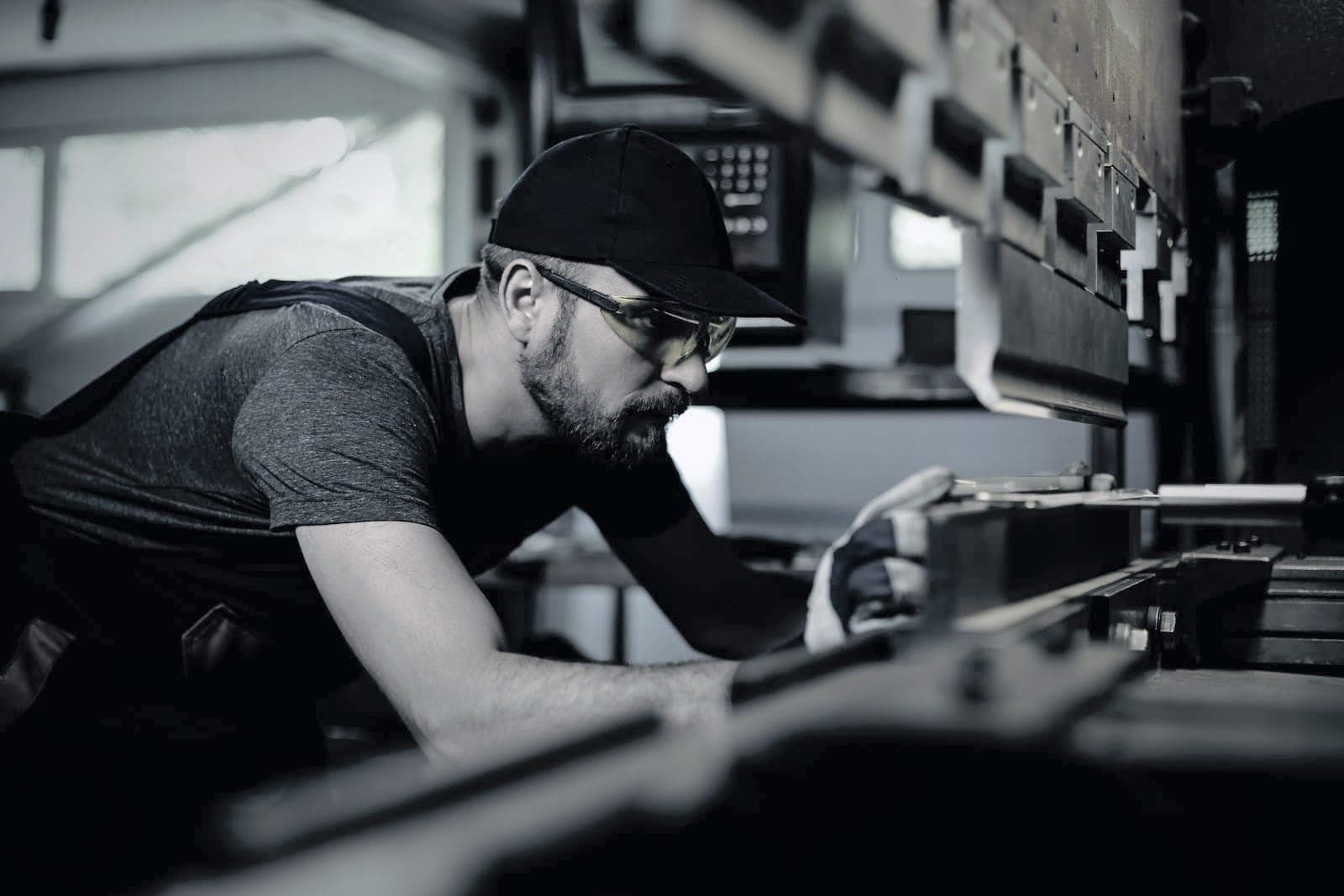 Press brake operator in a cap and safety glasses setting a blank under the punch