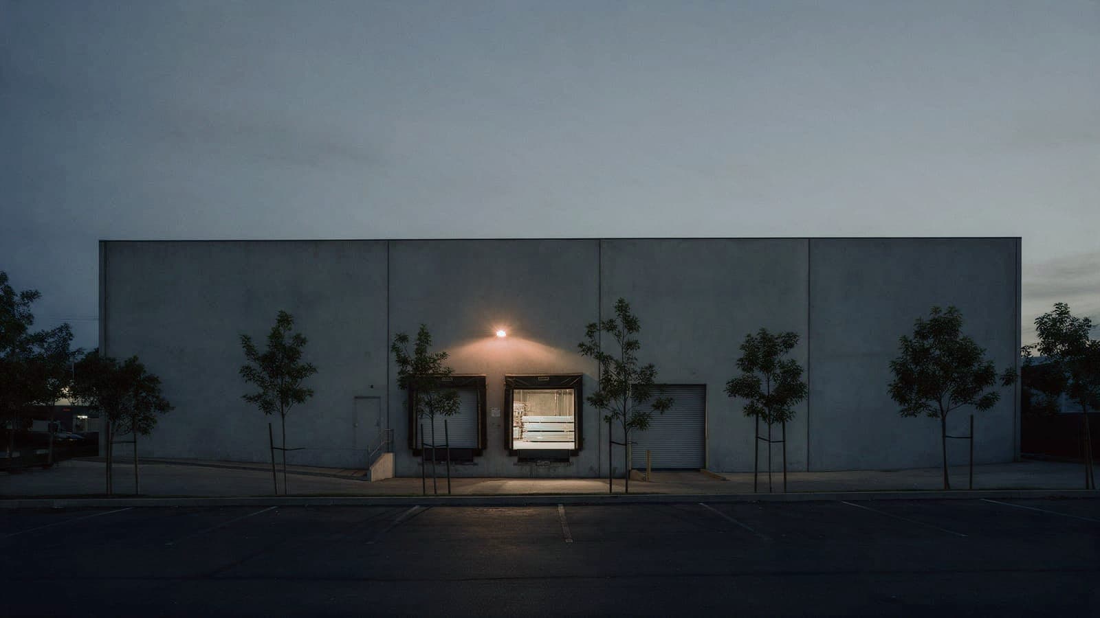The shop at blue hour: a plain concrete building with one dock door open and lit