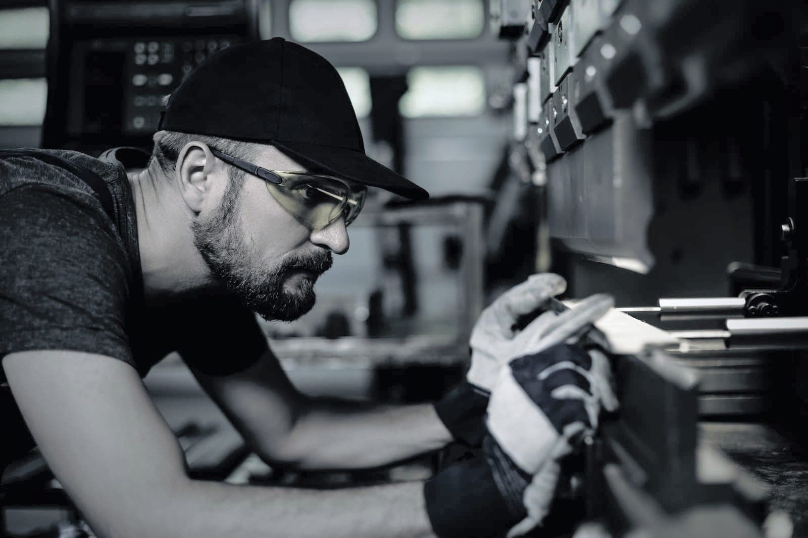 Operator in safety glasses squaring a blank against the backgauge under the punch, gloved hands on the sheet