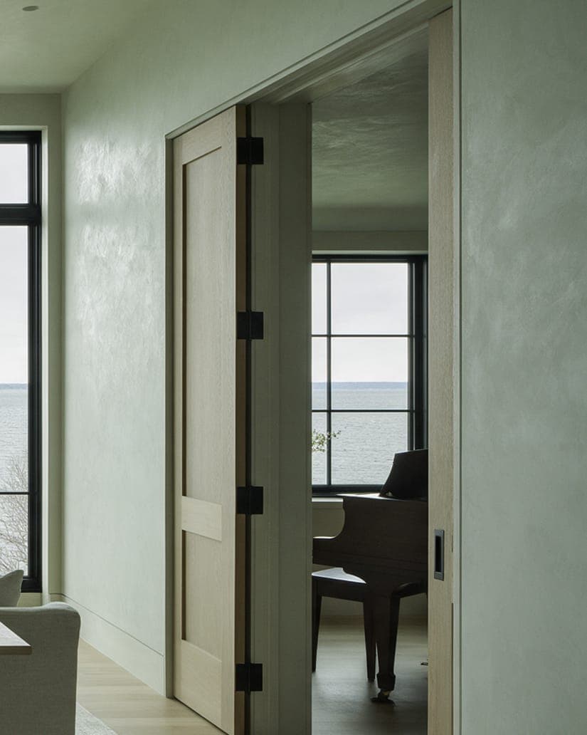 A grand piano seen through a pair of oak doors off the dining room at Bluff House.