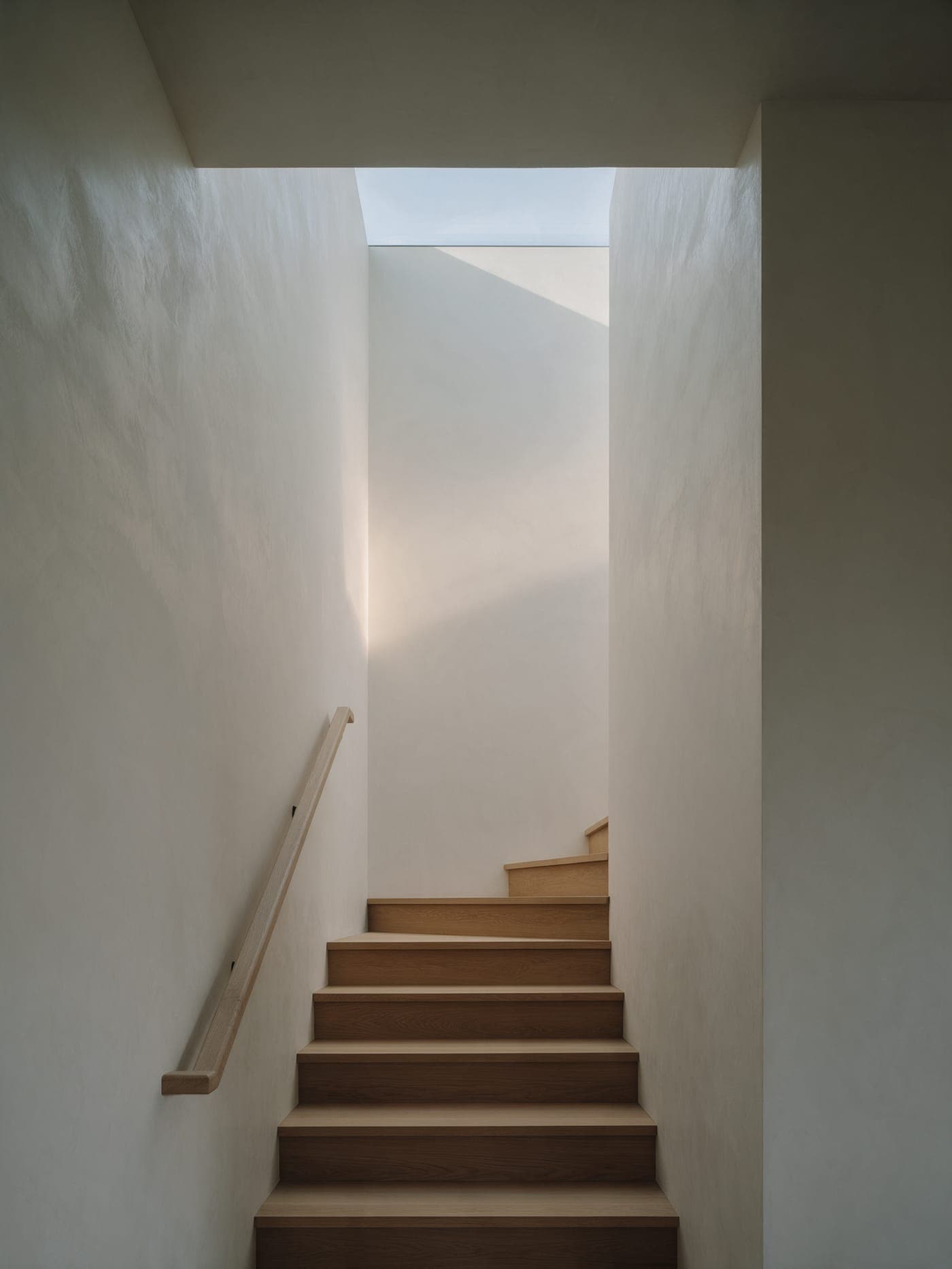 The stair hall at Bluff House: white oak treads climbing between lime plaster walls toward a skylight.