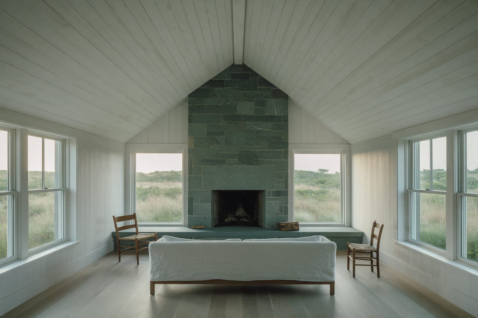 The living room under the middle gable of Dune Shingle House: board ceiling, a bluestone hearth, windows on three sides.