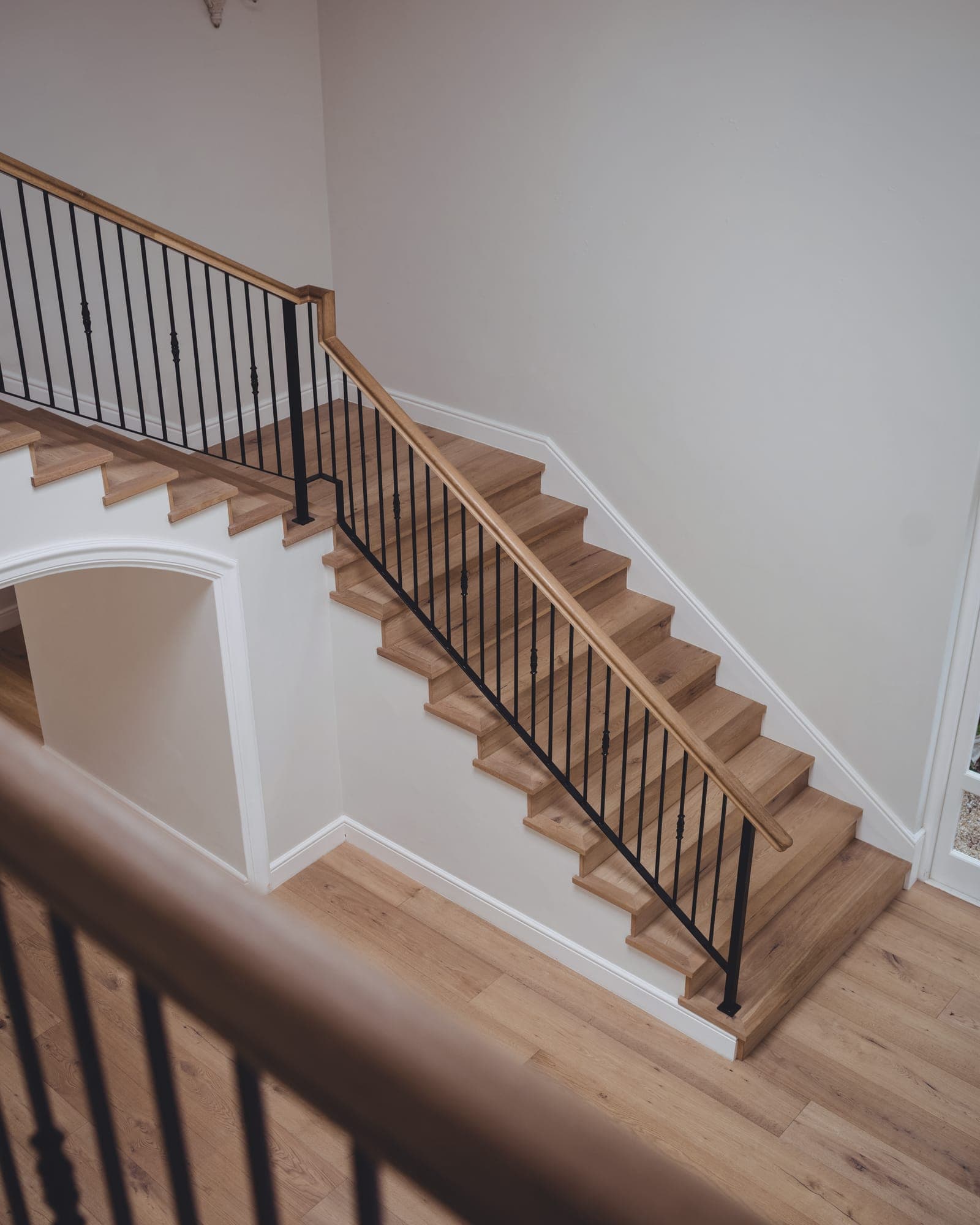 The stair at Gable Pair seen from the landing above: oak treads and handrail, black iron balusters, white walls and an arch under the run.