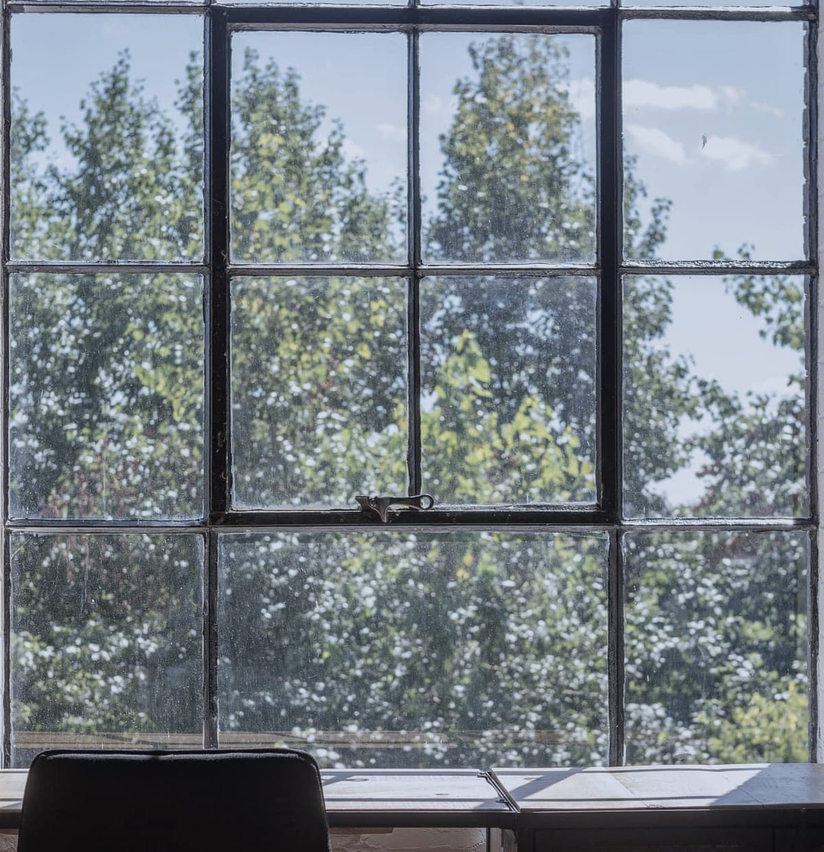 A desk and chair at a steel-framed window upstairs at Kettle House, the glass full of leaves.
