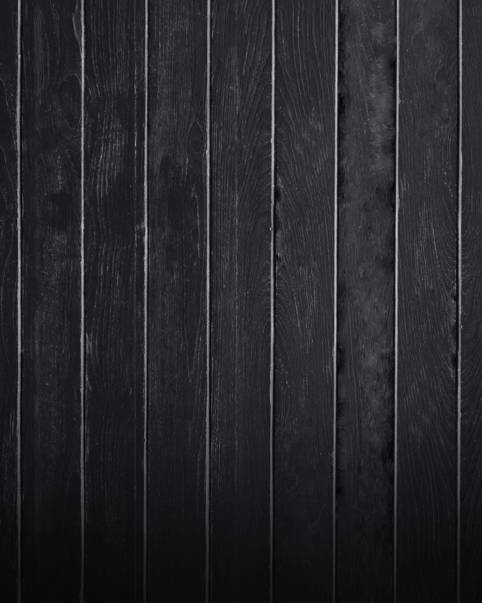Black-stained vertical boards up close, the grain showing through the stain.