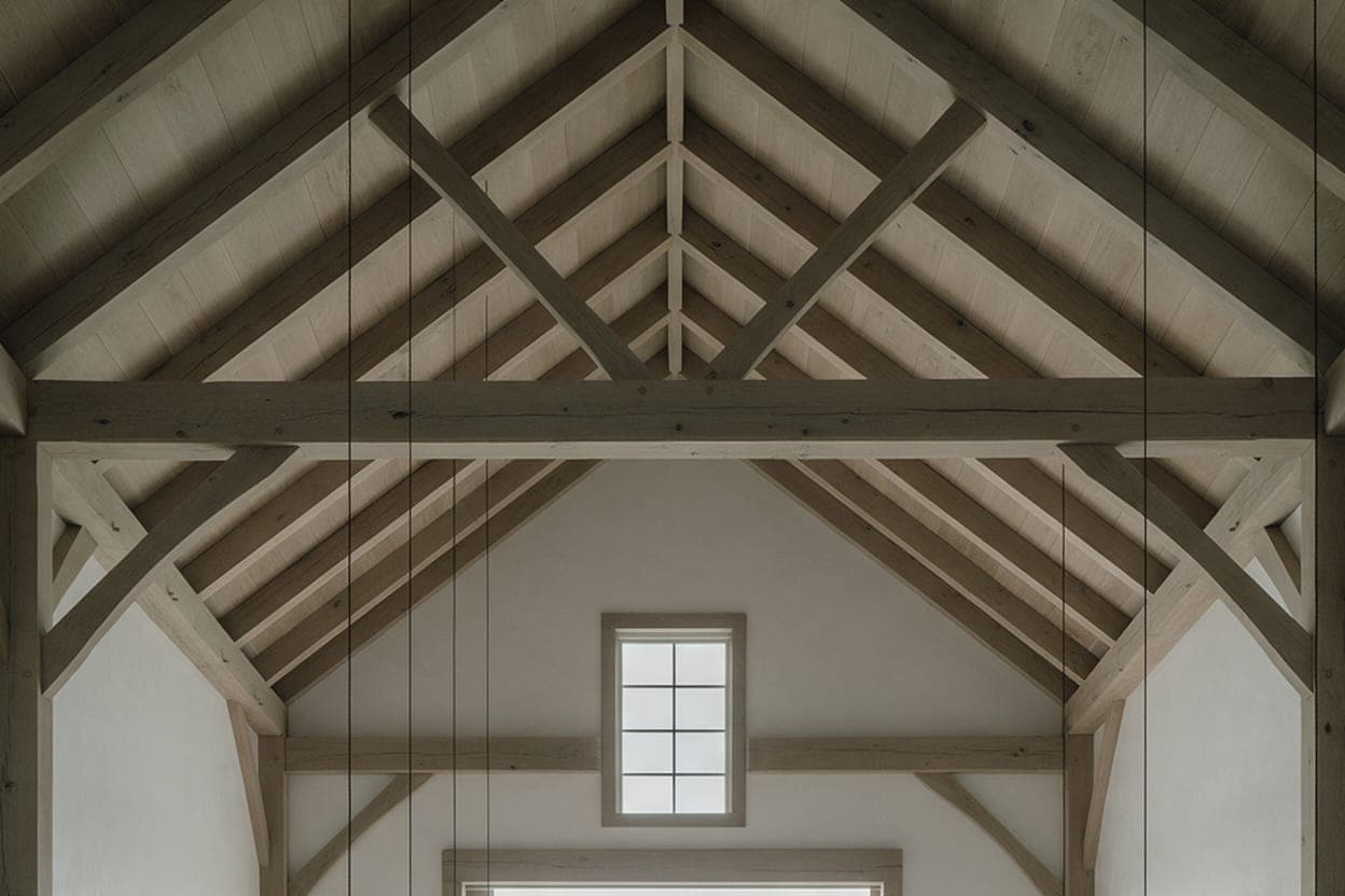 The timber frame over the main room of the Vineyard Barn House: pegged posts, knee braces and a tie beam under the rafters, a small window high in the gable.