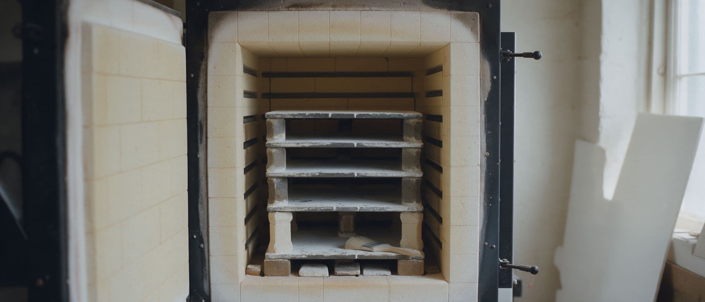 The empty kiln, shelves dusted with kiln wash