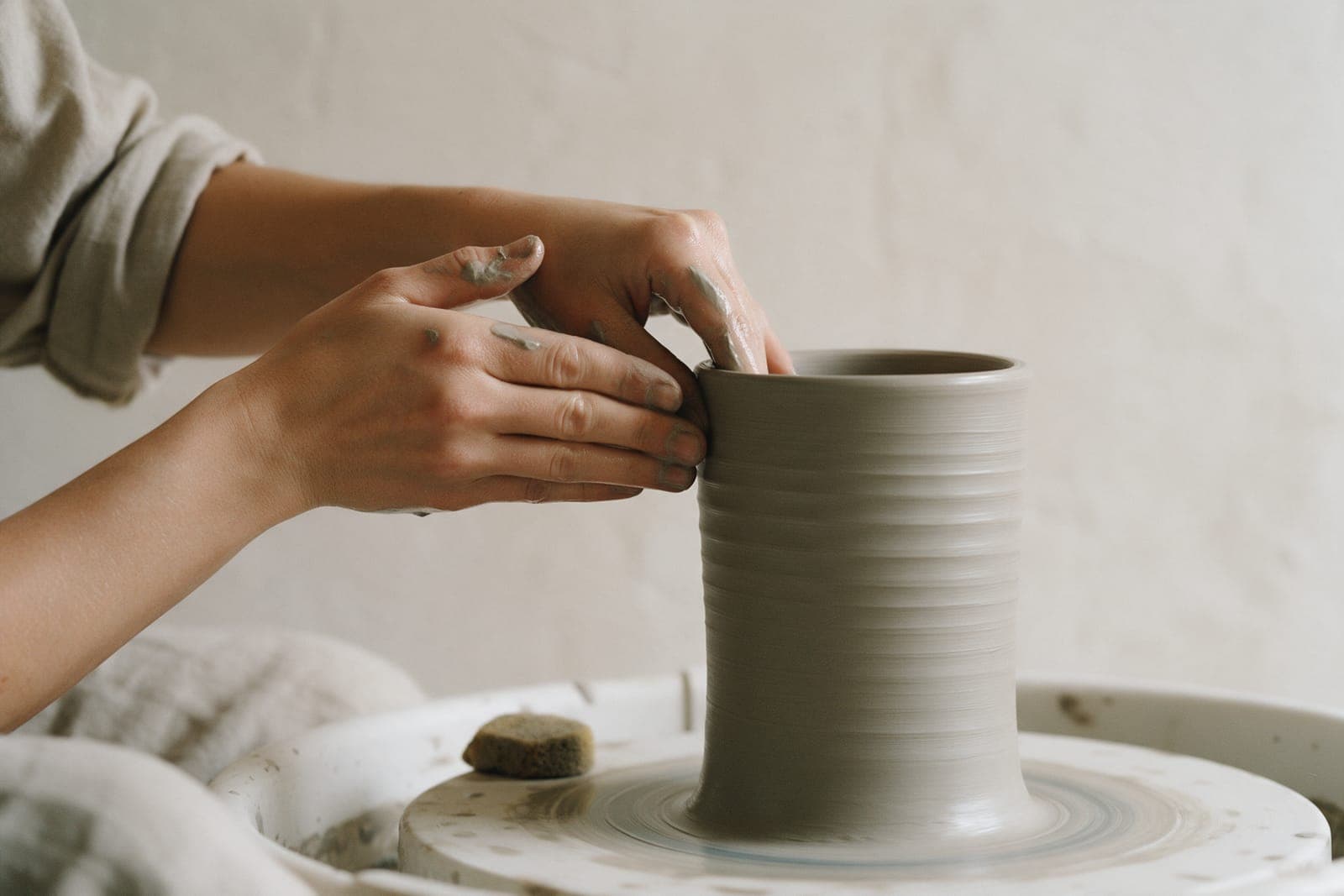 Hands pulling up the wall of a stoneware cylinder on the wheel