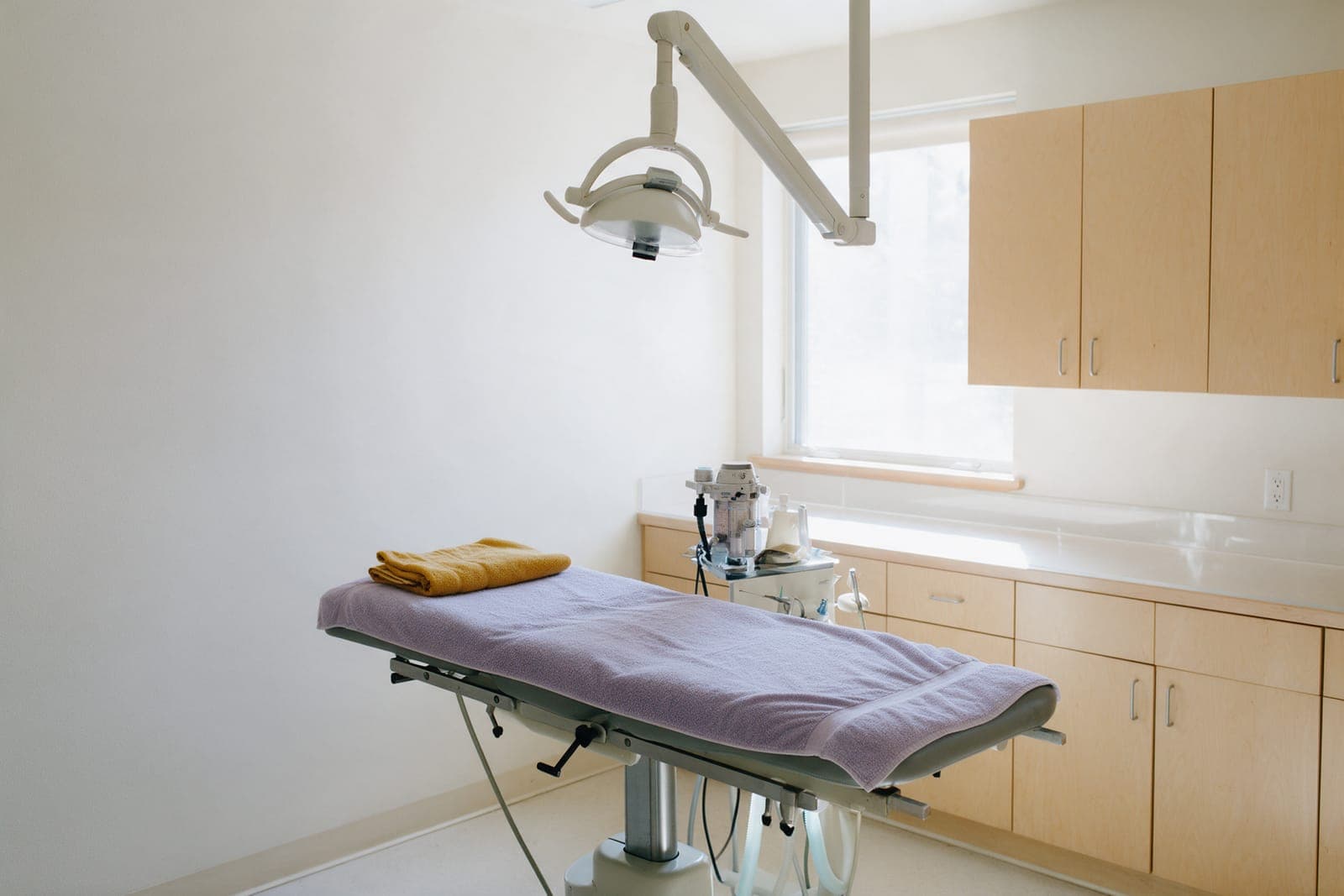 The dental suite: a padded table under a lavender towel, the dental light, and a tidy counter.