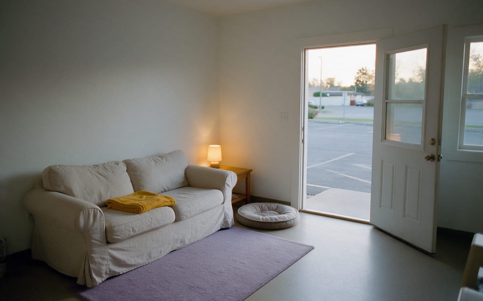 The quiet room: a linen sofa, one lamp, a dog bed, and its own door open to the parking lot.