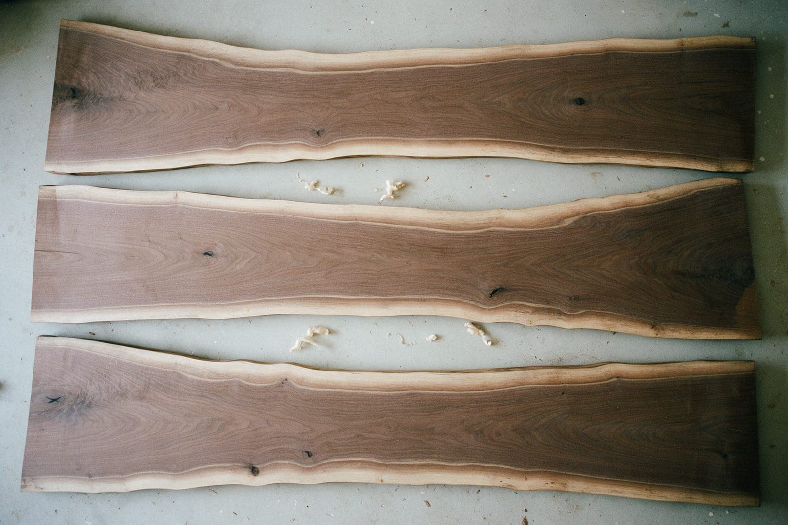 Three live-edge walnut slabs side by side on the shop floor, seen from above. Slab B is chalked for the boards, 60 by 22 cm.