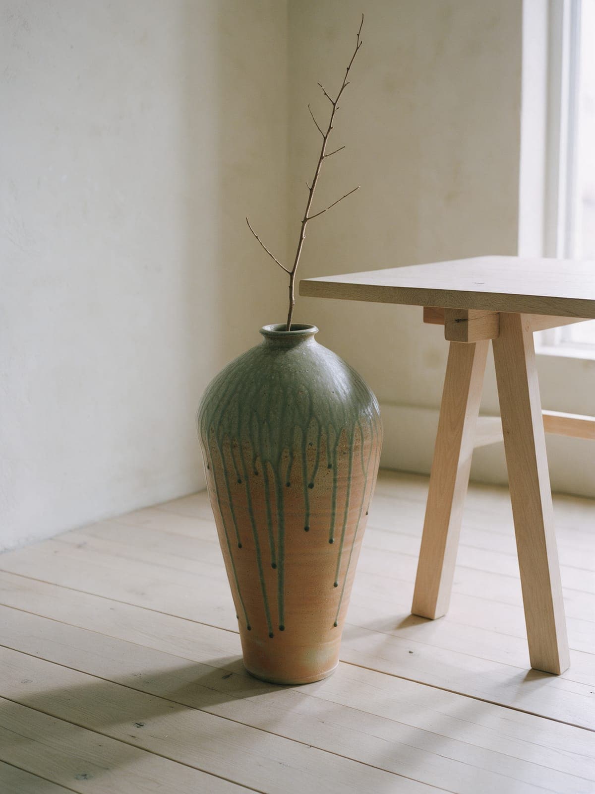 The Floor Vessel on oak floorboards by the end of the trestle table, one bare branch in it