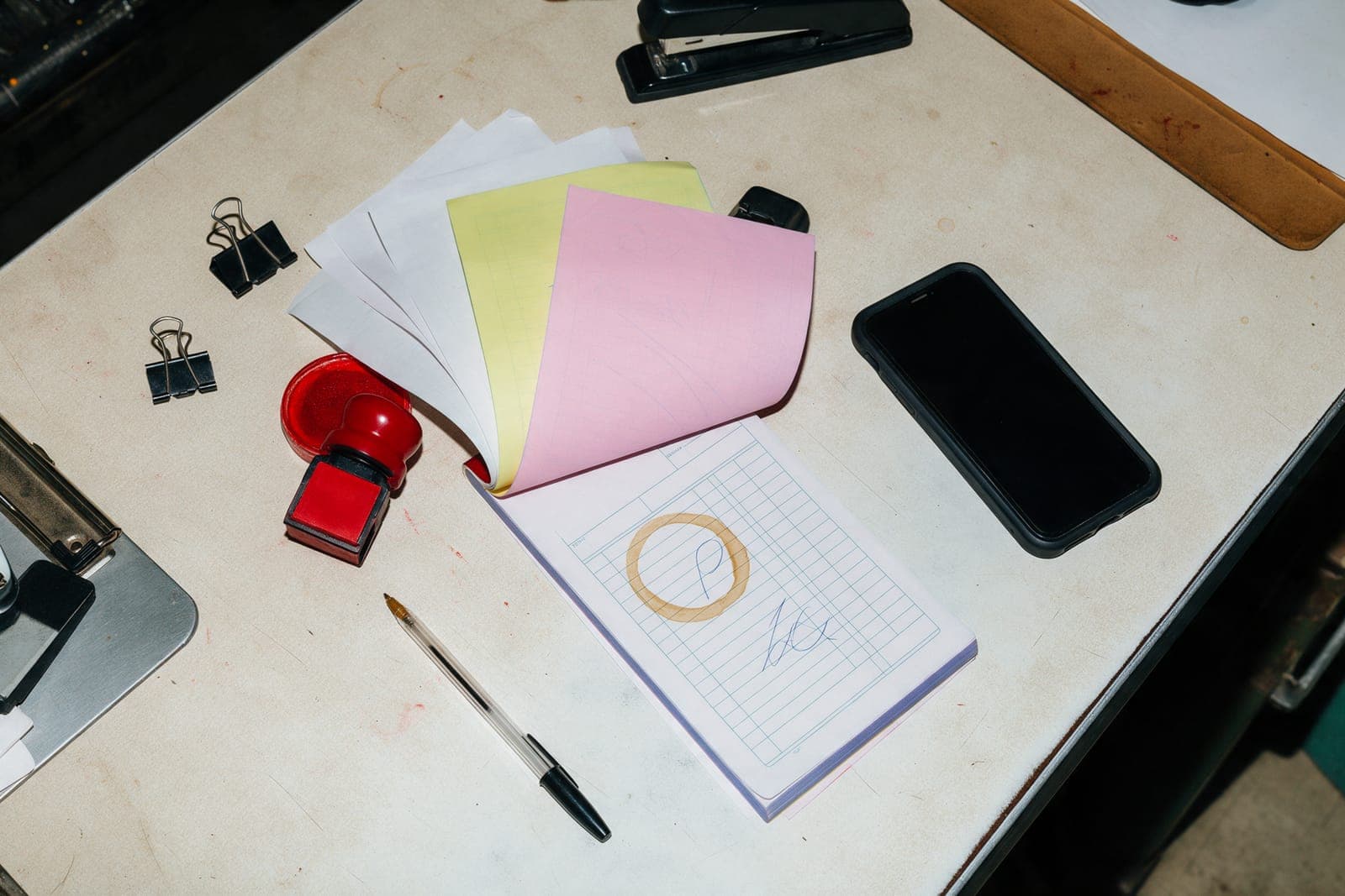 A contractor's desk from above: a triplicate estimate pad fanned out in white, yellow and pink, a rubber stamp, a phone and a coffee ring.