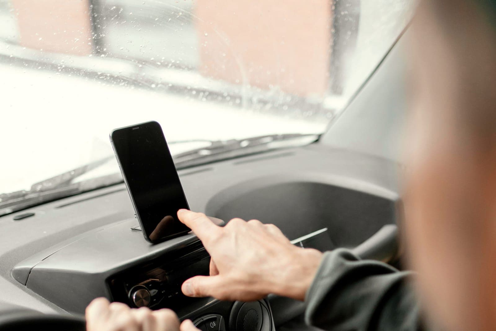 Inside a work van on a rainy morning: a phone in a dashboard mount and a finger tapping it.