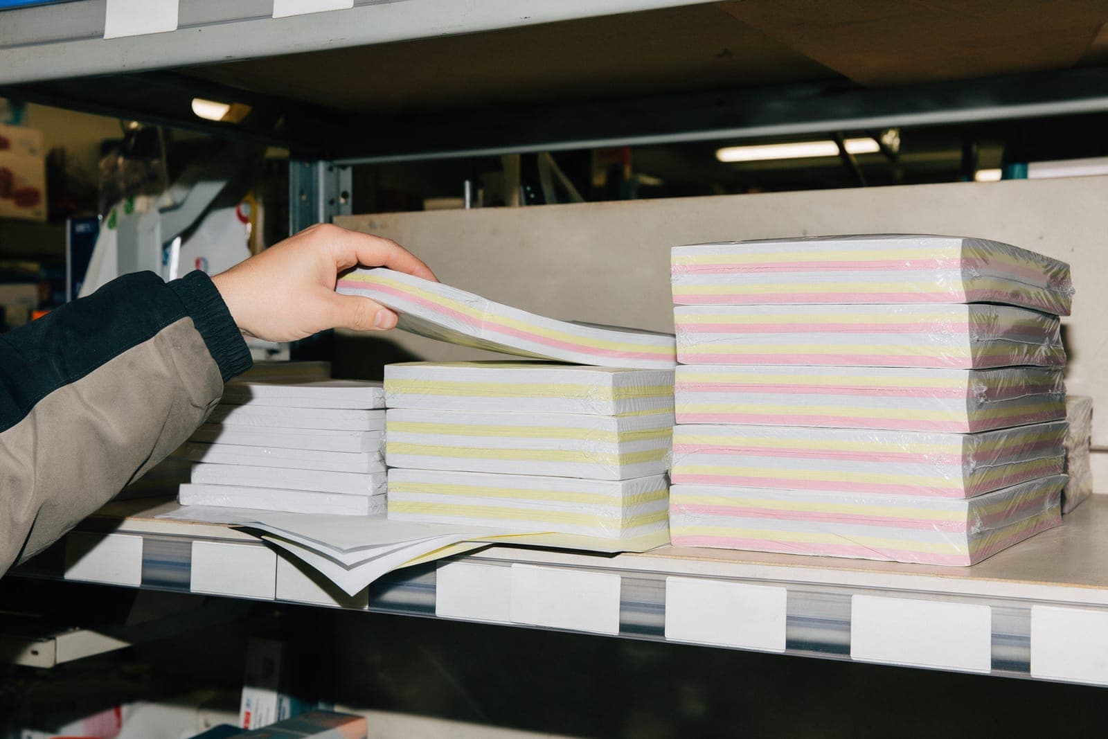 Shrink-wrapped carbonless pads on a supply-house shelf, their white, canary and pink edges showing as stripes.