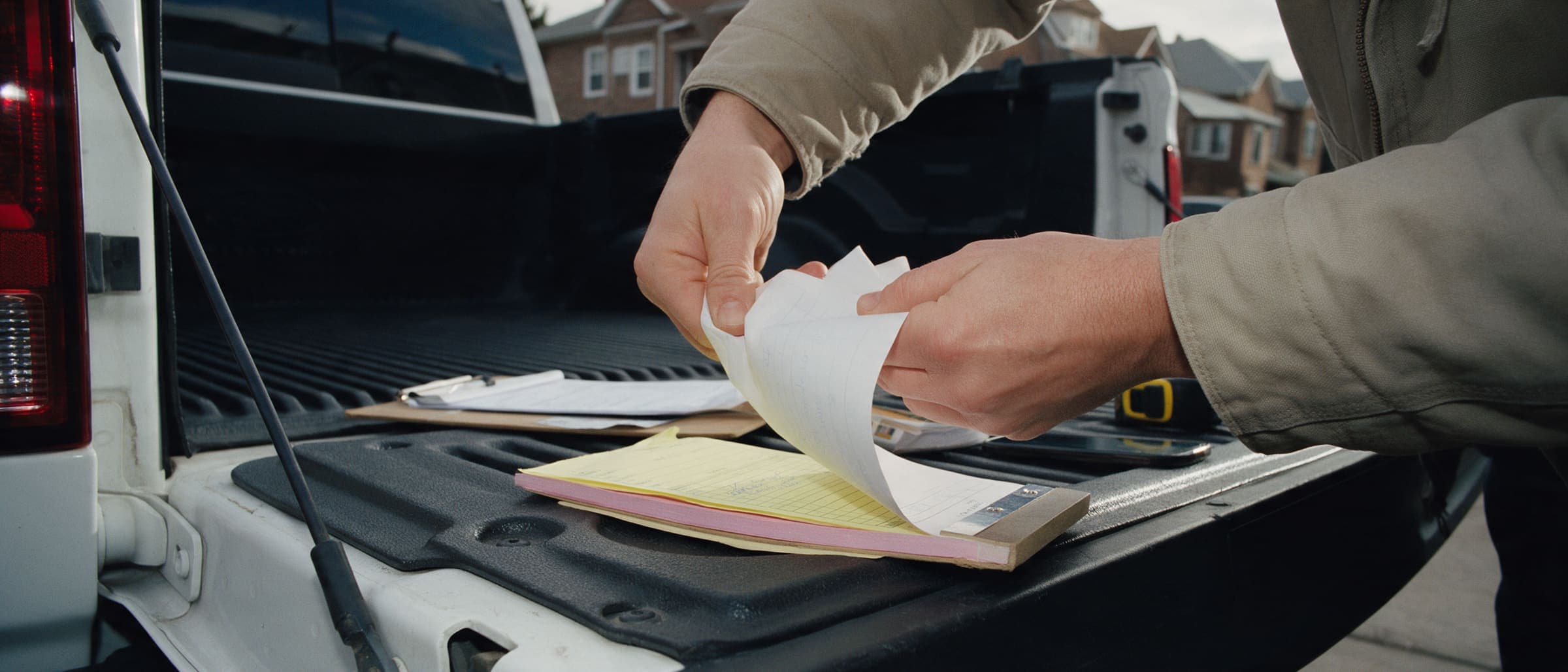Two hands tearing the white copy off a carbonless estimate pad on a pickup tailgate in a Queens driveway.