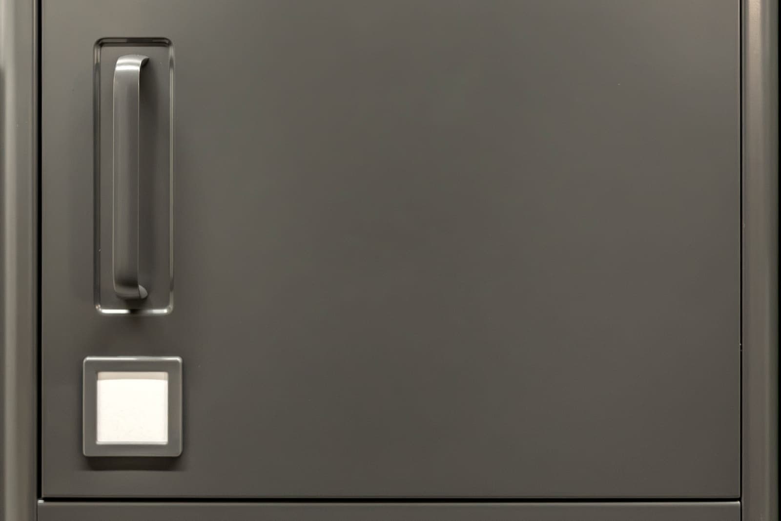 A grey steel cabinet door with a recessed handle and a blank label holder.