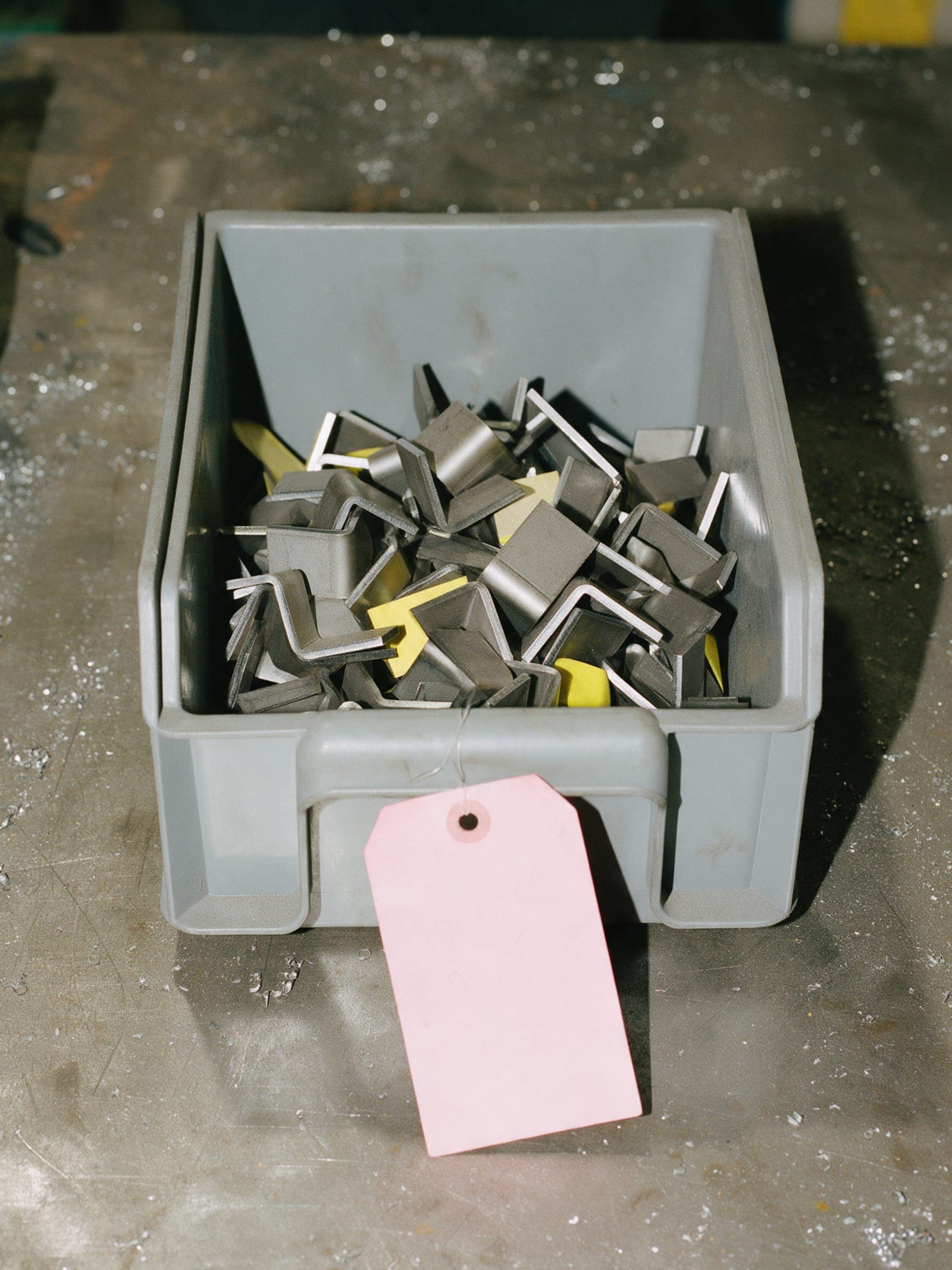 Cut steel brackets in a bin with a pink traveler tag.
