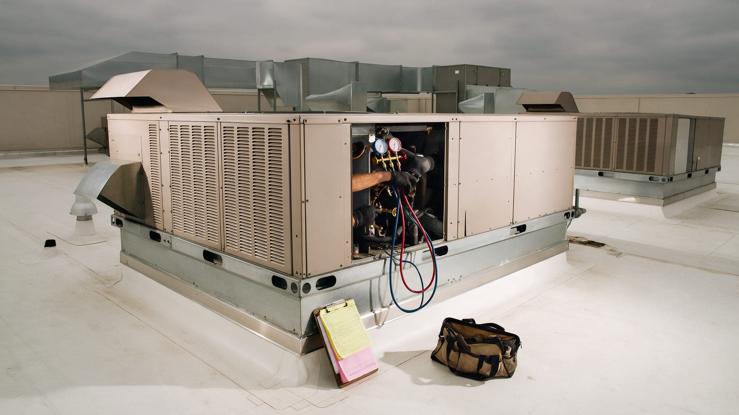 A technician inspecting a commercial rooftop unit with an estimate pad.