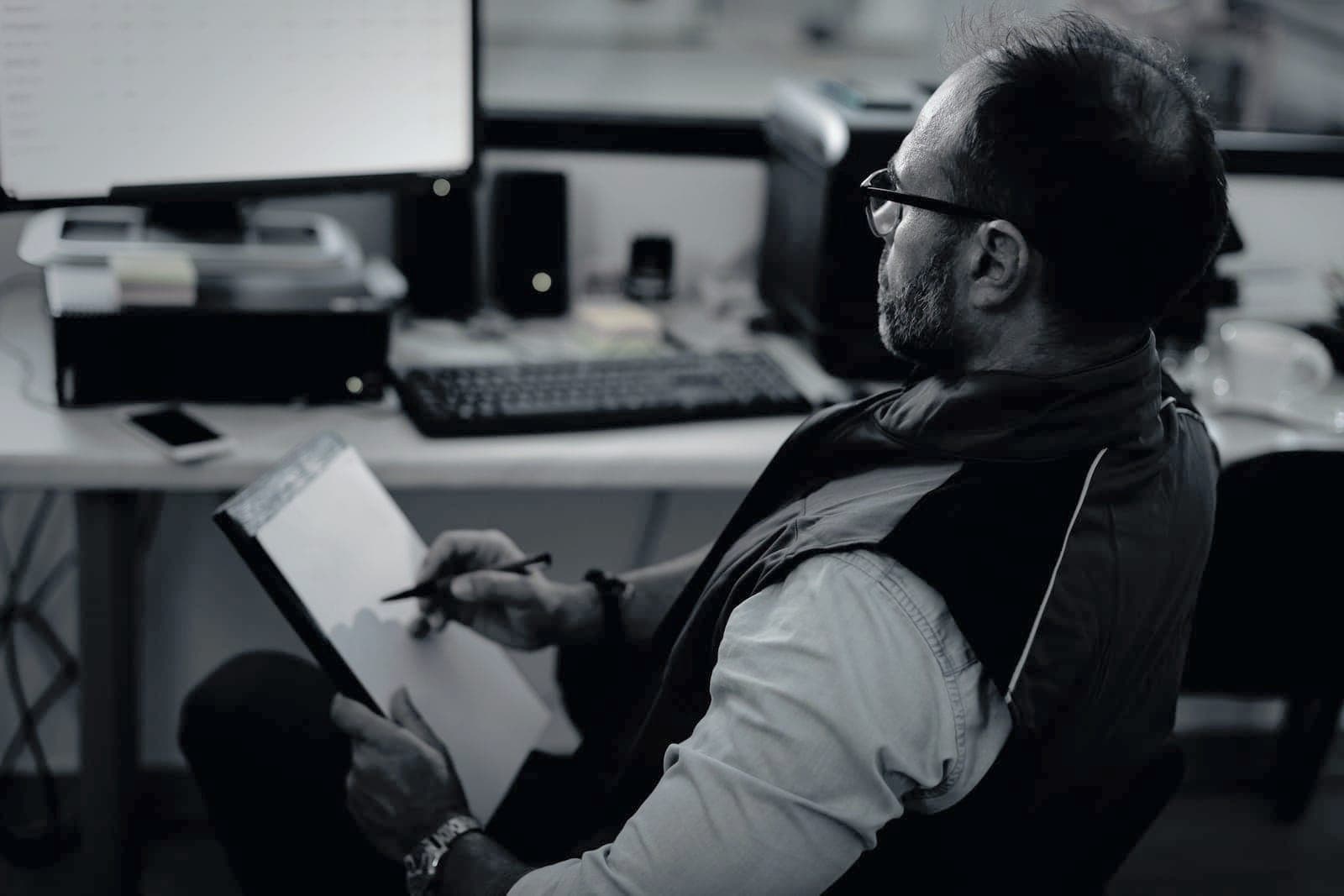 Estimator at the quote desk, clipboard in hand, reading a quote sheet on the monitor