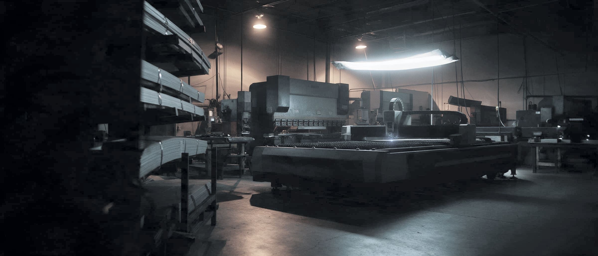 Dark fabrication shop floor with cutting and forming equipment, second shift
