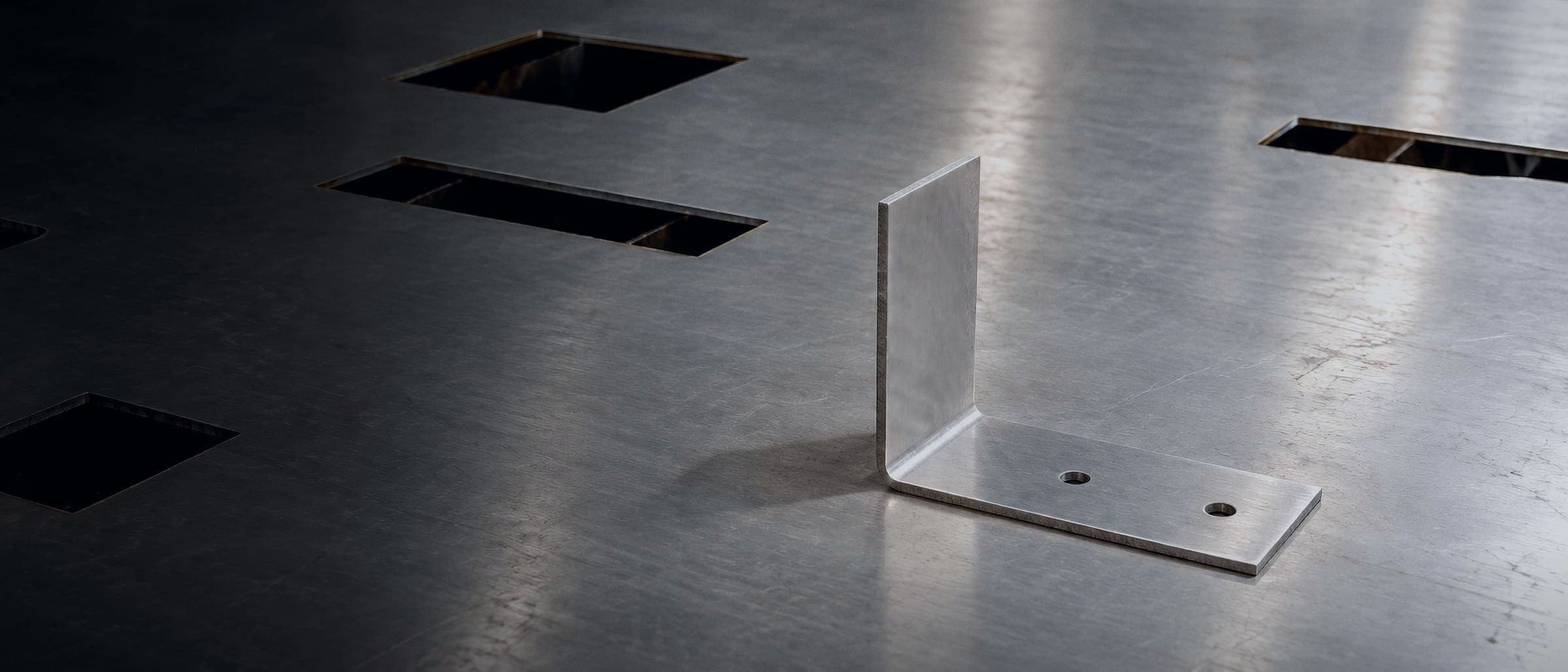 FW-1042, a formed aluminum L-bracket, lying on a freshly cut sheet on the laser bed, with its engineering print drawn over it