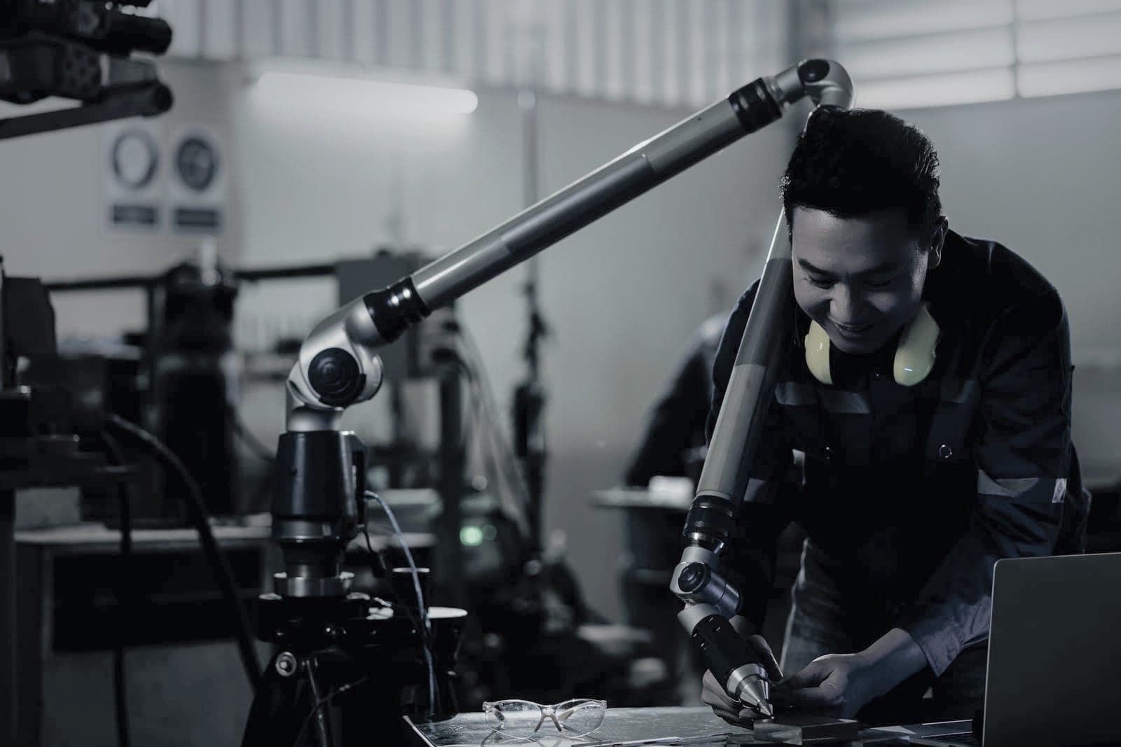 Inspector guiding a portable measuring arm onto a machined part, a laptop open beside the plate