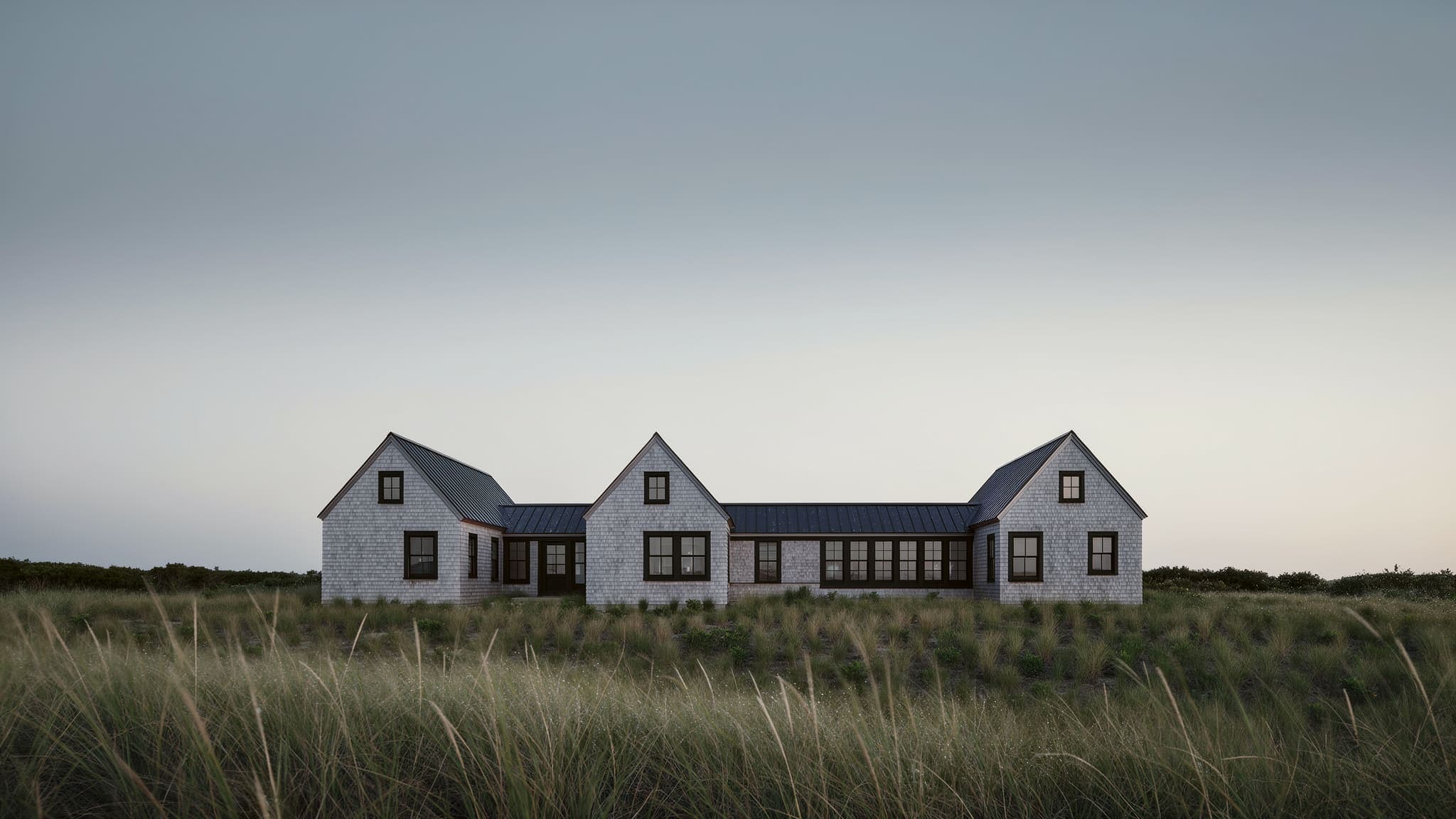 Dune Shingle House at dawn: the three shingled gables in soft early light, a pale sky and dew on the dune grass.