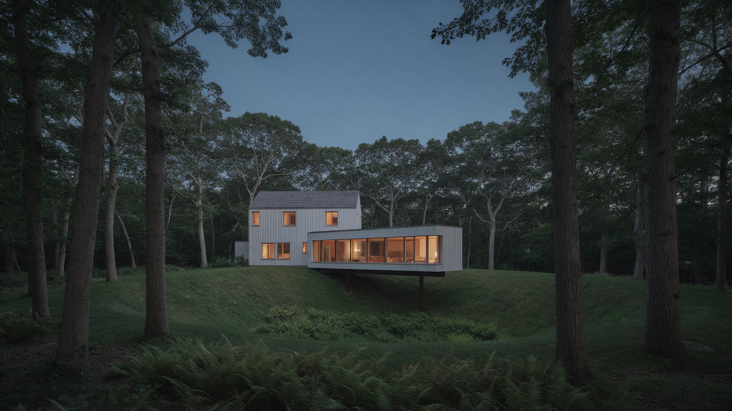 Kettle House in the oak woods at dusk, its glazed living room reaching out over the rim of the hollow on steel beams.