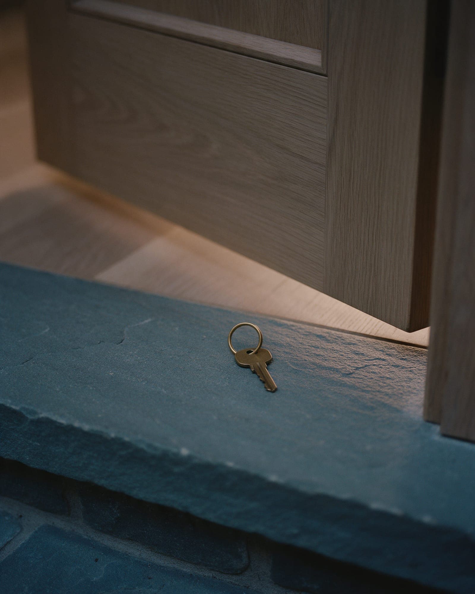 A brass key on a bluestone threshold in front of an oak door standing just open.