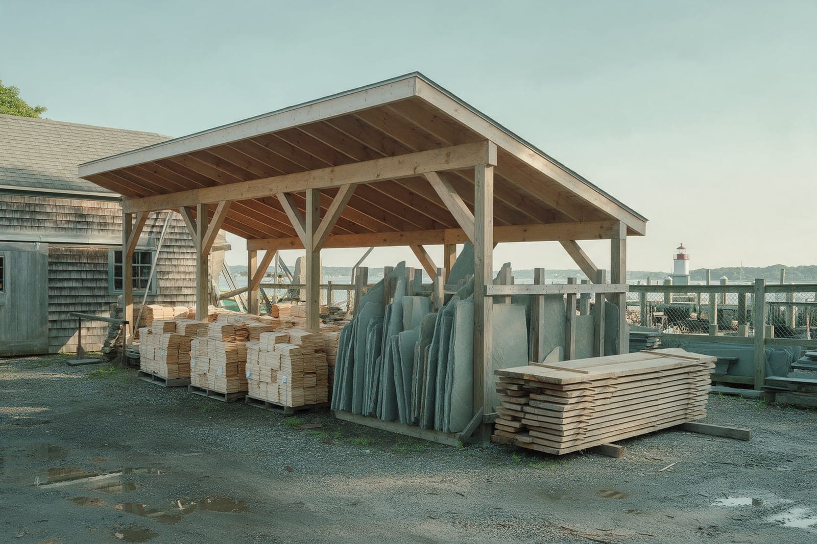 The yard behind the shed: cedar shingle bundles under an open timber lean-to, bluestone slabs on edge in a rack and stickered oak boards.