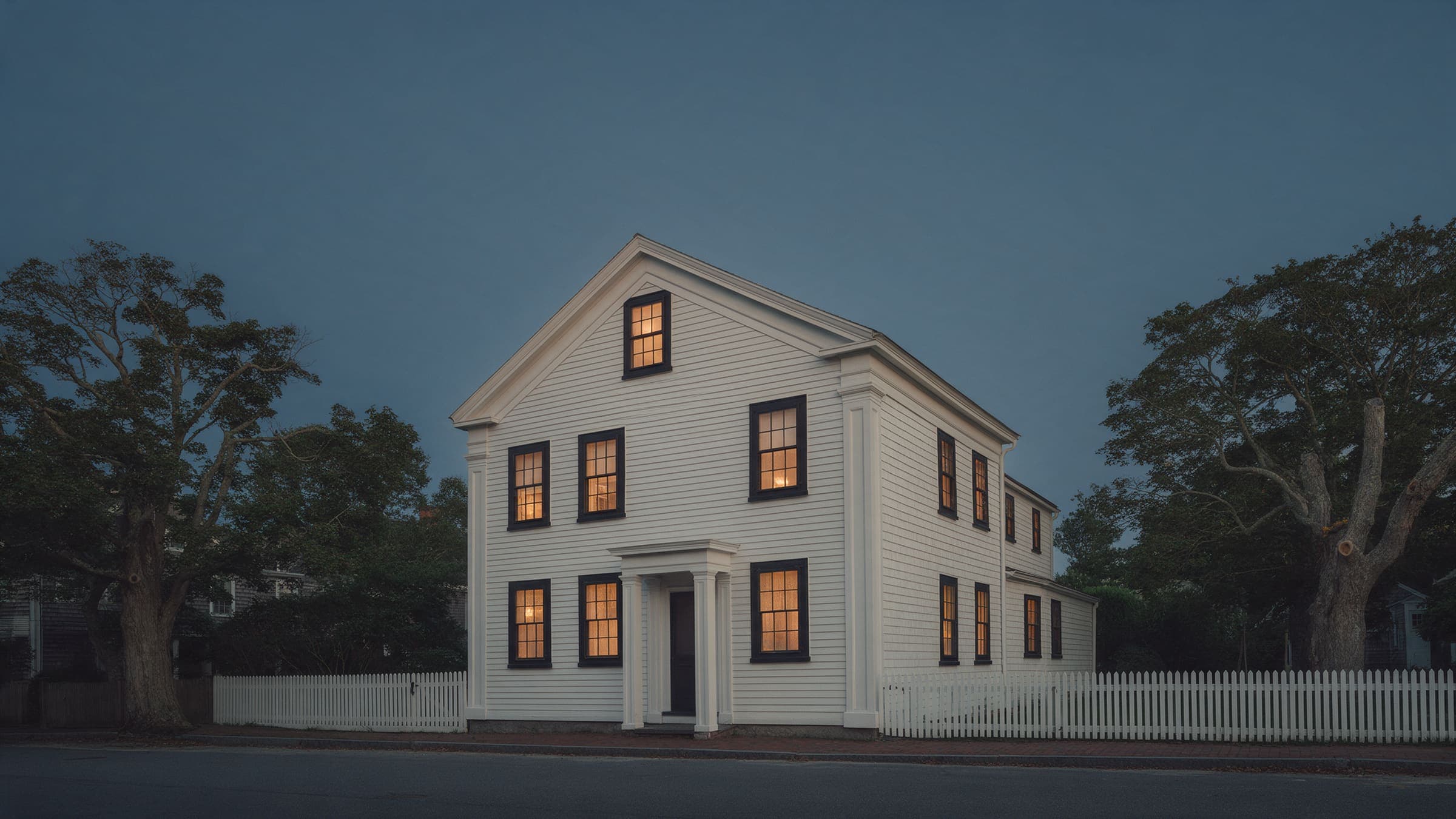 Whaler's Cottage from the street at dusk: a white clapboard Greek Revival house with black sash windows and a picket fence.
